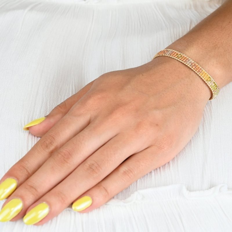 cette mini manchette élégante est composée de 3 rangs de perles nude, dorées et roses poudrées, créant un design doux et féminin. . Bijou porté, Crédit GEMITY.