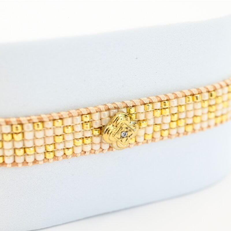 cette petite manchette délicate se compose de 5 rangs de perles nude et dorées, apportant une touche douce et lumineuse à votre poignet. Son ornement central en forme de lotus doré symbolise l’harmonie et la sérénité. . Bijou seul, Crédit GEMITY