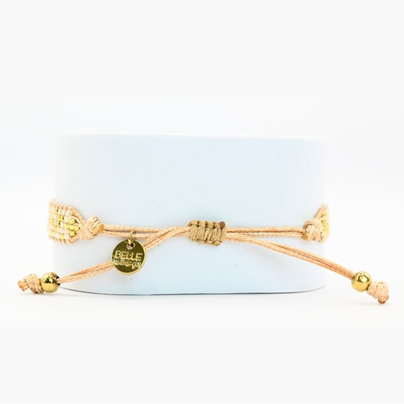 cette petite manchette délicate se compose de 5 rangs de perles nude et dorées, apportant une touche douce et lumineuse à votre poignet. Son ornement central en forme de lotus doré symbolise l’harmonie et la sérénité. . Bijou seul, Crédit GEMITY
