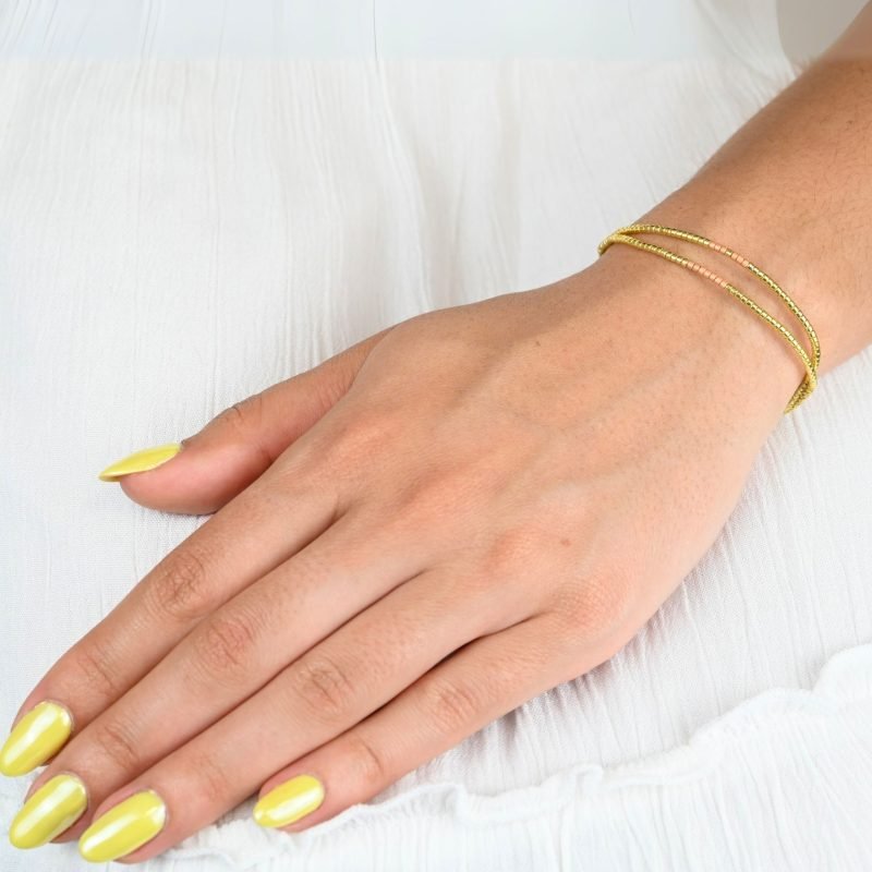 ce bracelet élégant combine harmonieusement des cordes fines au début et des perles dorées et rose poudré en son centre. . Bijou porté, Crédit GEMITY.