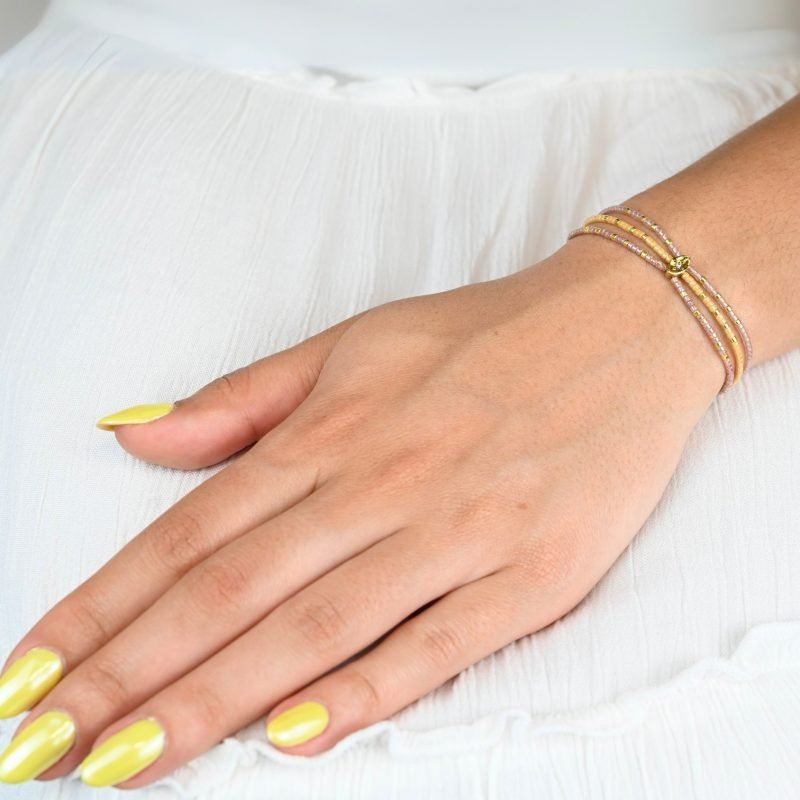 ce bracelet fin à 3 rangs regroupe des perles dorées et nude, créant un effet raffiné et élégant. L'ornement central rassemble les rangs pour un look harmonieux et sophistiqué. . Bijou porté, Crédit GEMITY.