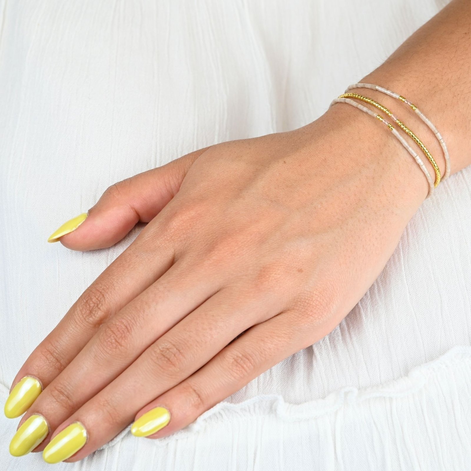 ce bracelet élégant à 3 rangs combine des perles dorées sur le premier rang et des perles blanches sur les deux autres, créant un look raffiné et lumineux. . Bijou porté, Crédit GEMITY.
