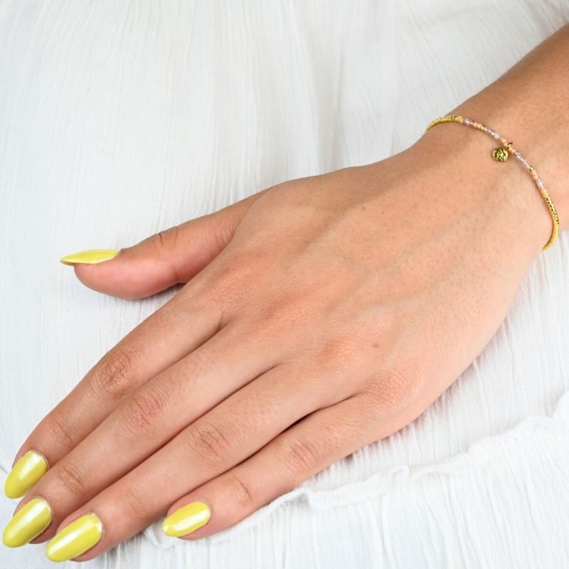 ce bracelet fin au design délicat est le parfait accessoire pour apporter une touche d’élégance subtile à votre poignet. Composé de perles dorées et nude, il se distingue par un charm ovale qui ajoute une note de raffinement. . Bijou porté, Crédit GEMITY.