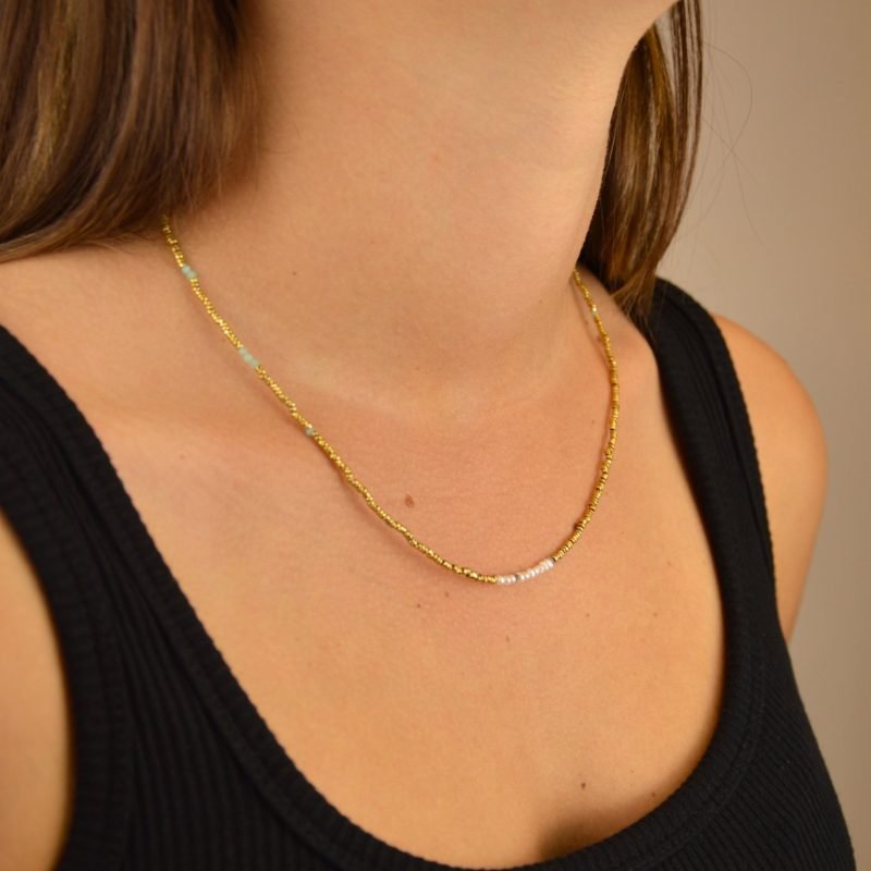 Ce bijou polyvalent se compose de petites perles dorées subtilement mises en valeur par quelques perles en nacre placées en son centre. . Bijou porté, Crédit GEMITY.