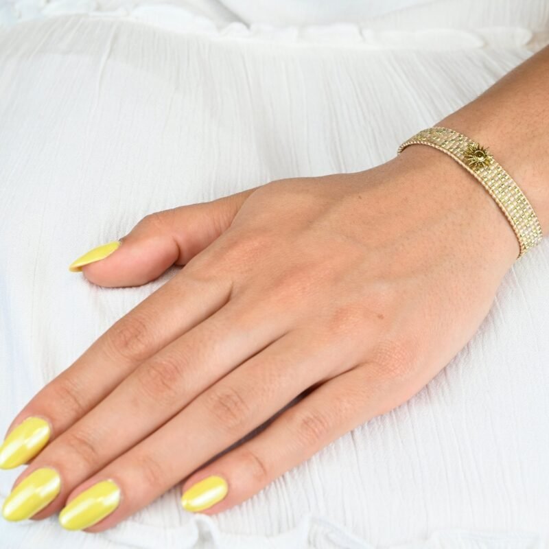 apportez une touche de luminosité à votre poignet avec cette petite manchette élégante. Composée de 5 rangs de perles dorées et nude, elle crée un contraste subtil et raffiné. L'ornement soleil au centre ajoute une note chaleureuse et scintillante, évoquant l’éclat du jour.. Bijou porté, Crédit GEMITY.