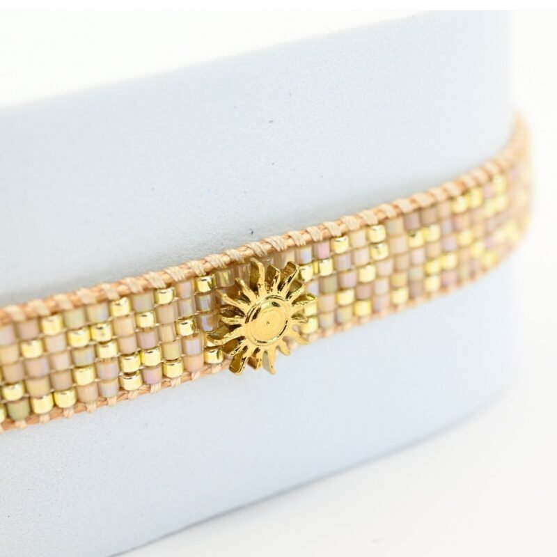 apportez une touche de luminosité à votre poignet avec cette petite manchette élégante. Composée de 5 rangs de perles dorées et nude, elle crée un contraste subtil et raffiné. L'ornement soleil au centre ajoute une note chaleureuse et scintillante, évoquant l’éclat du jour.. Bijou seul, Crédit GEMITY