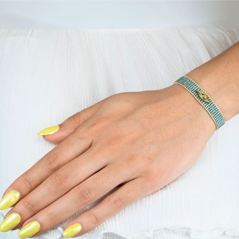 apportez une touche de mystère et de style à votre poignet avec cette petite manchette élégante, composée de 5 rangs de perles vertes vibrantes. L'ornement œil en son centre ajoute une dimension symbolique et unique à ce bijou.. Bijou porté, Crédit GEMITY.