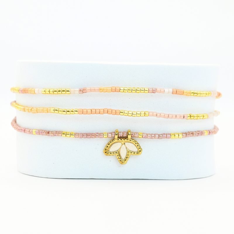 ce bracelet fin à 3 rangs associe des perles dorées, nude et dans les tons rosés pour un effet doux et élégant. Il est orné d’un charm fleur de lotus en nacre, posé sur un fond doré de la même forme, apportant une touche de raffinement et de luminosité. . Bijou seul, Crédit GEMITY