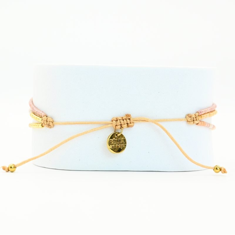 ce bracelet fin à 3 rangs associe des perles dorées, nude et dans les tons rosés pour un effet doux et élégant. Il est orné d’un charm fleur de lotus en nacre, posé sur un fond doré de la même forme, apportant une touche de raffinement et de luminosité. . Bijou seul, Crédit GEMITY