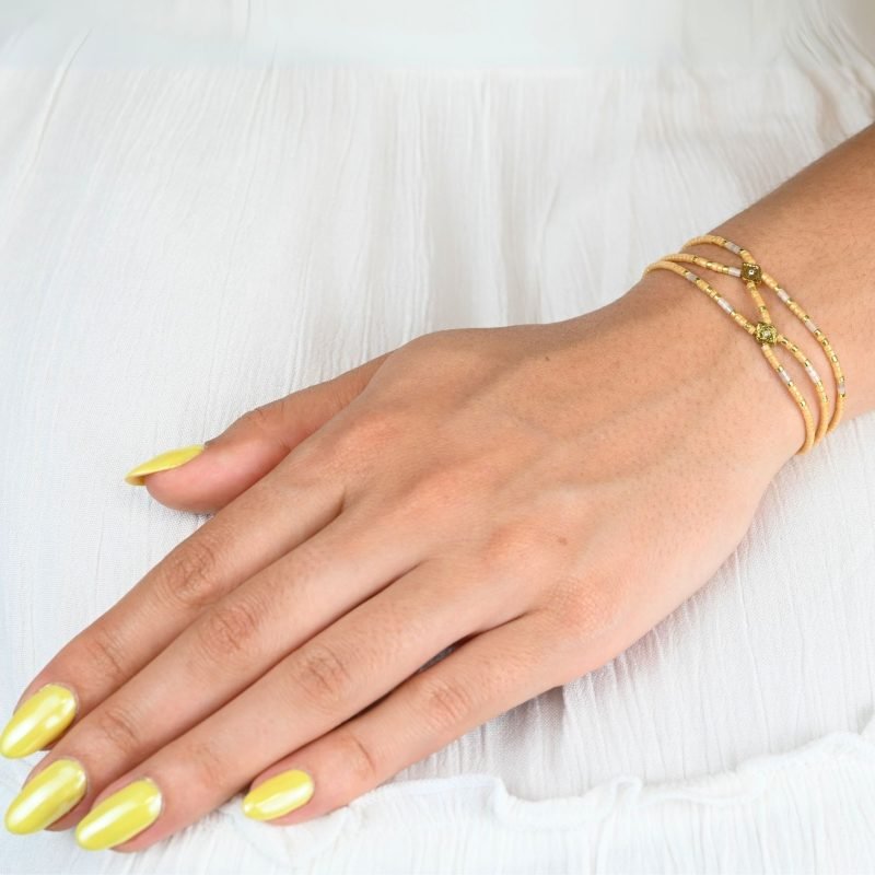 ce bracelet fin à 3 rangs associe des perles dorées et nude, créant un look élégant et discret. Les rangs sont réunis par deux ornements délicats, ajoutant une touche supplémentaire de raffinement et de structure. . Bijou porté, Crédit GEMITY.
