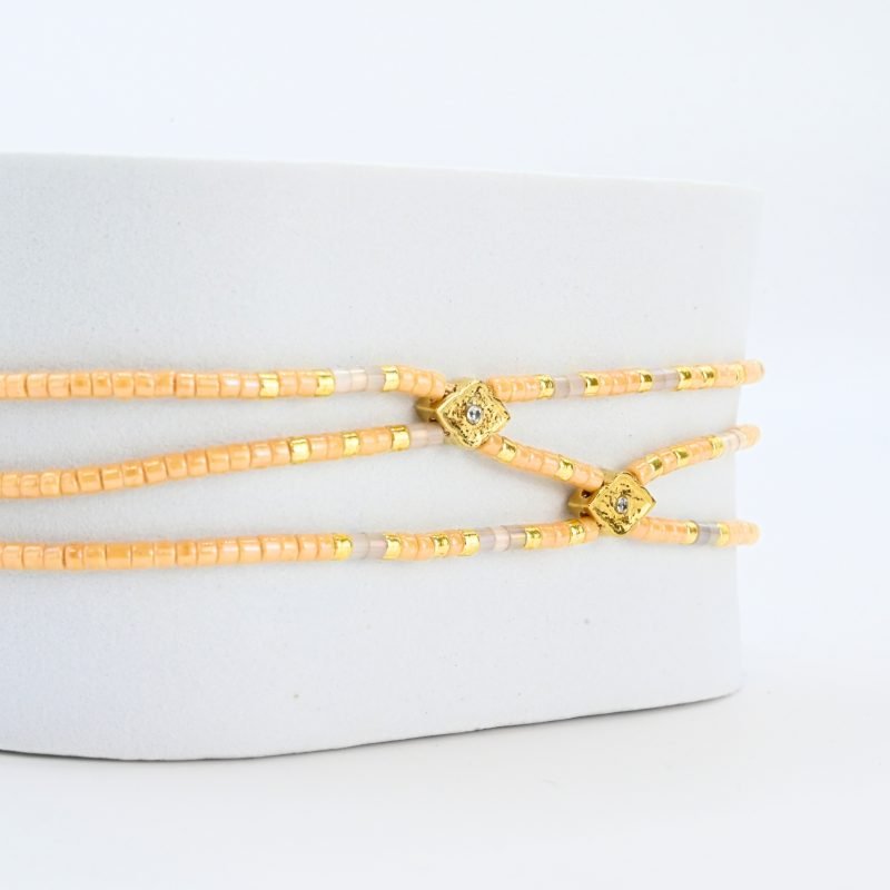 ce bracelet fin à 3 rangs associe des perles dorées et nude, créant un look élégant et discret. Les rangs sont réunis par deux ornements délicats, ajoutant une touche supplémentaire de raffinement et de structure. . Bijou seul, Crédit GEMITY