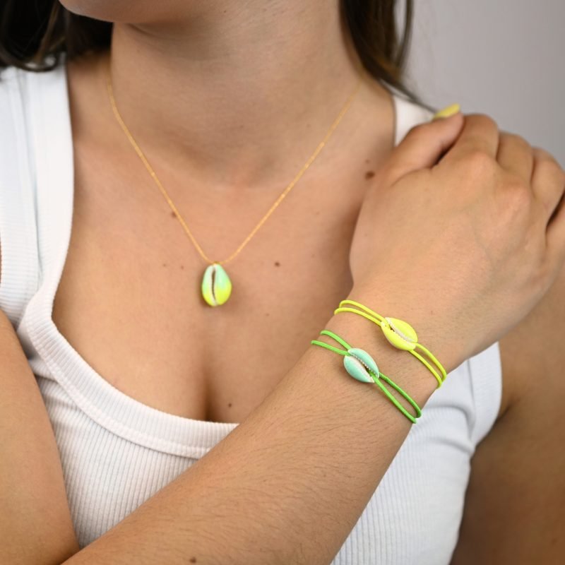"Véritable cauri émaillé (longueur ≈ 1,5 cm) de la même couleur que le cordon. Lien cordon en coton ajustable, convient pour des poignets de 14 à 19 cm.. Bijou porté, Crédit GEMITY."