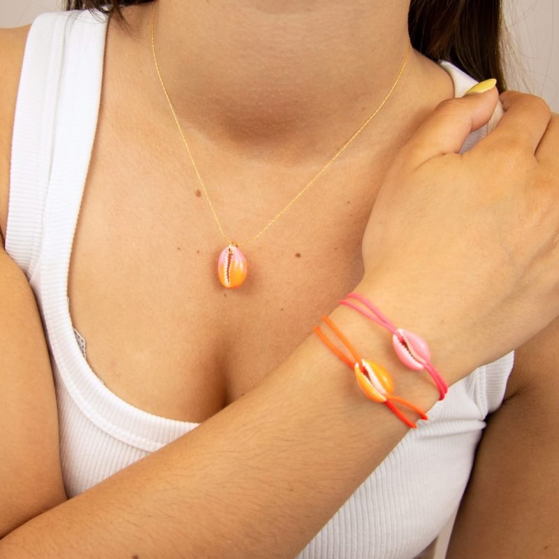 "Véritable cauri émaillé (longueur ≈ 1,5 cm) de la même couleur que le cordon. Lien cordon en coton ajustable, convient pour des poignets de 14 à 19 cm.. Bijou porté, Crédit GEMITY."