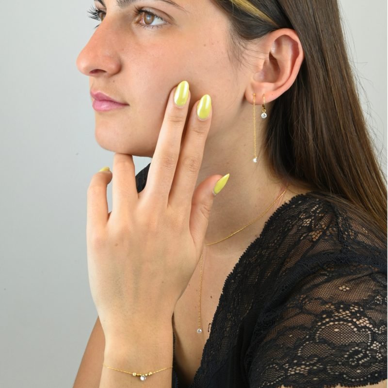 "Bracelet plaqué or (3 microns) avec un zirconium, entouré par des petites perles cylindriques en plaqué or, sur chaîne extra fine . Bijou porté, Crédit GEMITY."