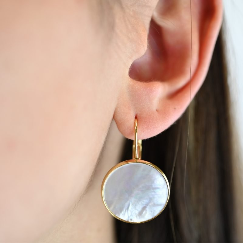 "Composition : boucles d’oreilles en métal et nacre naturelle. Caractéristiques : taille du pendant : 24 mm. Bijou porté, Crédit GEMITY."
