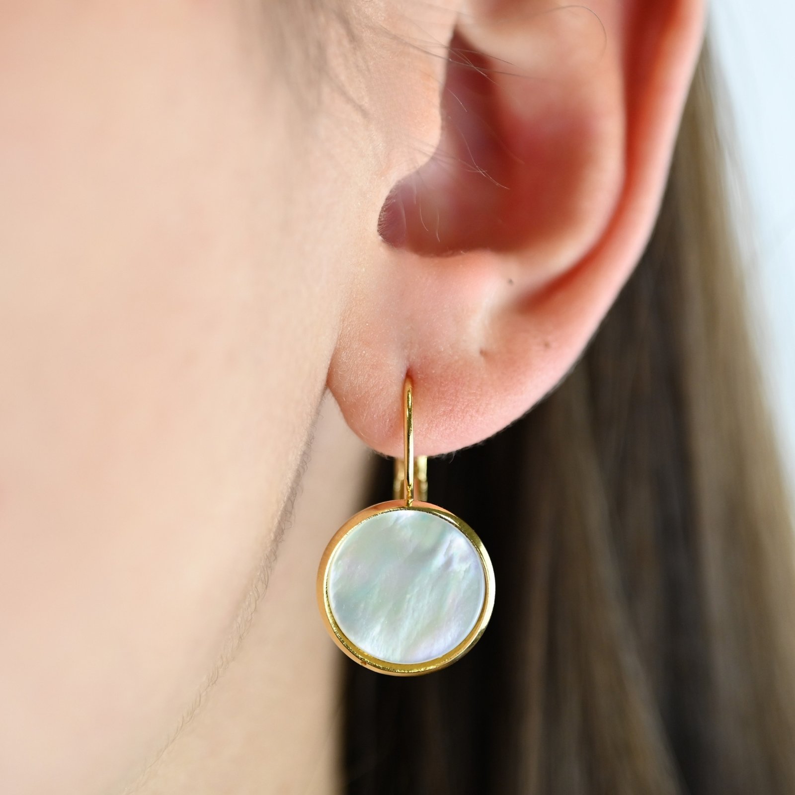 "Boucles d’oreilles dormeuses et cabochon en nacre de 14 mm. Elles sont dorées à l’or fin 24 carats. Ces boucles apporteront une touche lumineuse à vos tenues dans un style épuré. . Bijou porté, Crédit GEMITY."