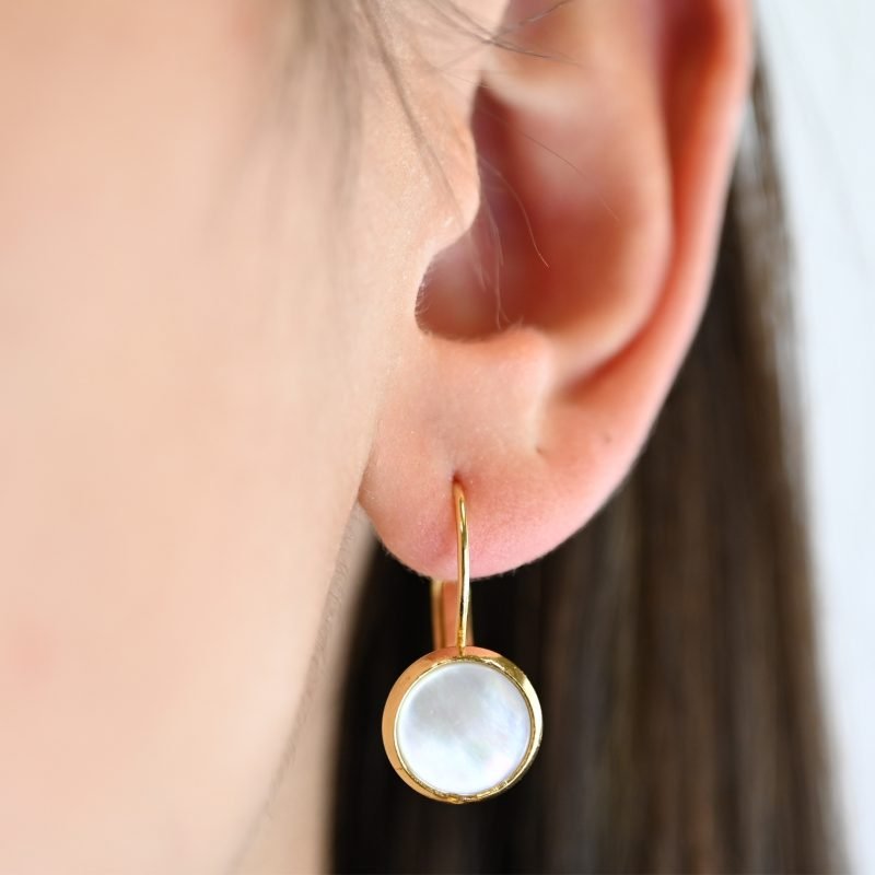 "Boucles d’oreilles dormeuse en métal plaqué or 24 carats. Composées d’un cabochon en nacre naturelle de 1 cm. Ce bijou apportera une touche lumineuse à vos tenues dans un style épuré. . Bijou porté, Crédit GEMITY."