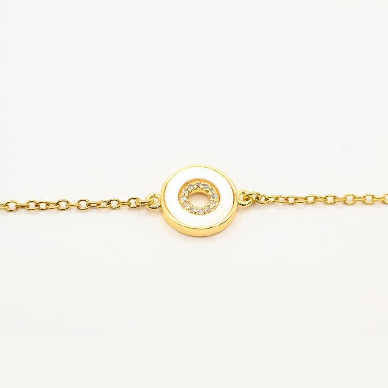 "Ce bracelet de 15 cm est en acier inoxydable et ajustable avec sa chaîne d’extension de 4 cm. Le motif central est de 1 cm et il est en nacre cerclée de métal et de zirconium. Ce bijou est doré à l’or fin 24 carats et il ne provoque pas d’allergies dues au nickel. . Bijou seul, Crédit GEMITY"