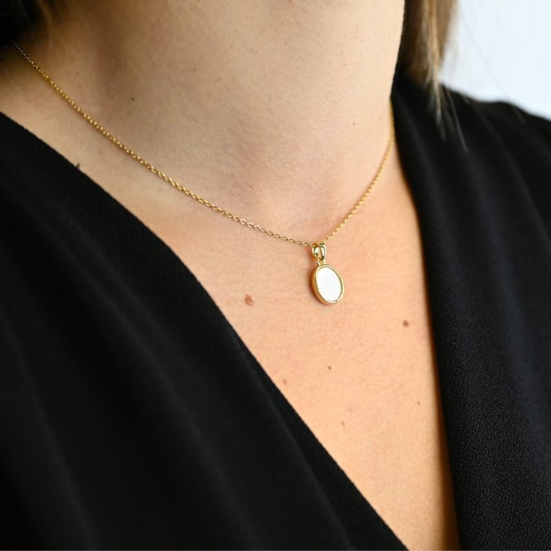 "Collier avec une nacre naturelle montée sur métal doré à l’or fin avec un pendentif en nacre ovale de 1 cm. La longueur de la chaîne est de 40 cm + chaînette de rallonge. . Bijou porté, Crédit GEMITY."