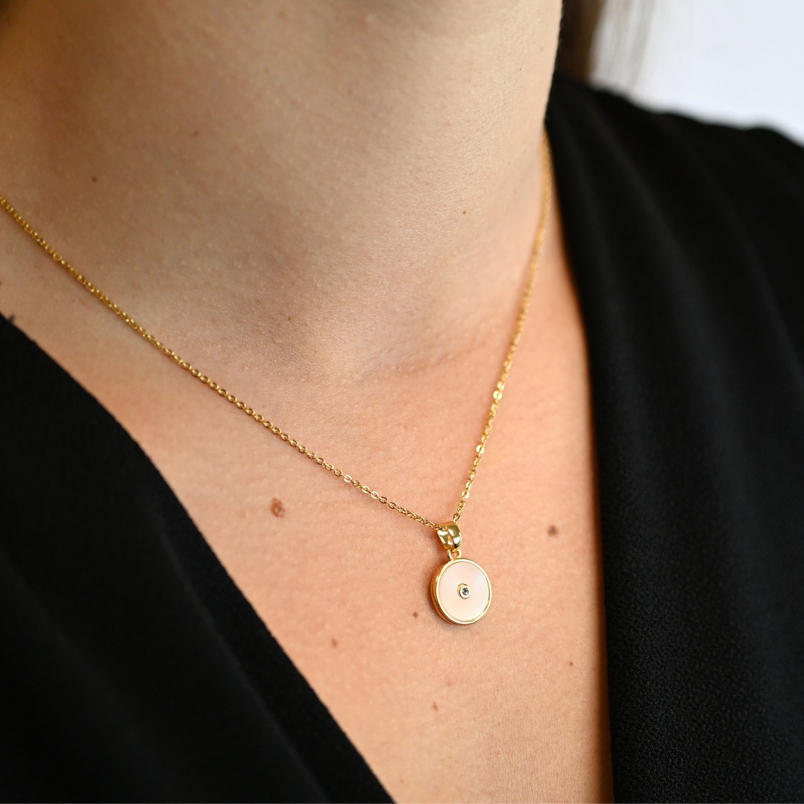 "Collier avec une nacre naturelle montée sur du métal doré à l’or fin 24 carats et cabochon en nacre qui mesure 1 cm de diamètre avec en son centre un petit zircon. La longueur de la chaîne est de 40 cm + chaînette de rallonge. . Bijou porté, Crédit GEMITY."