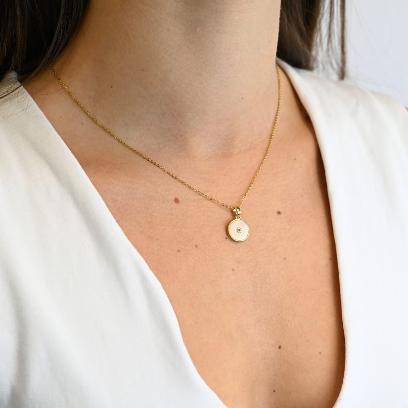 "Collier avec une nacre naturelle montée sur du métal doré à l’or fin 24 carats et cabochon en nacre qui mesure 1 cm de diamètre avec en son centre un petit zircon. La longueur de la chaîne est de 40 cm + chaînette de rallonge. . Bijou porté, Crédit GEMITY."