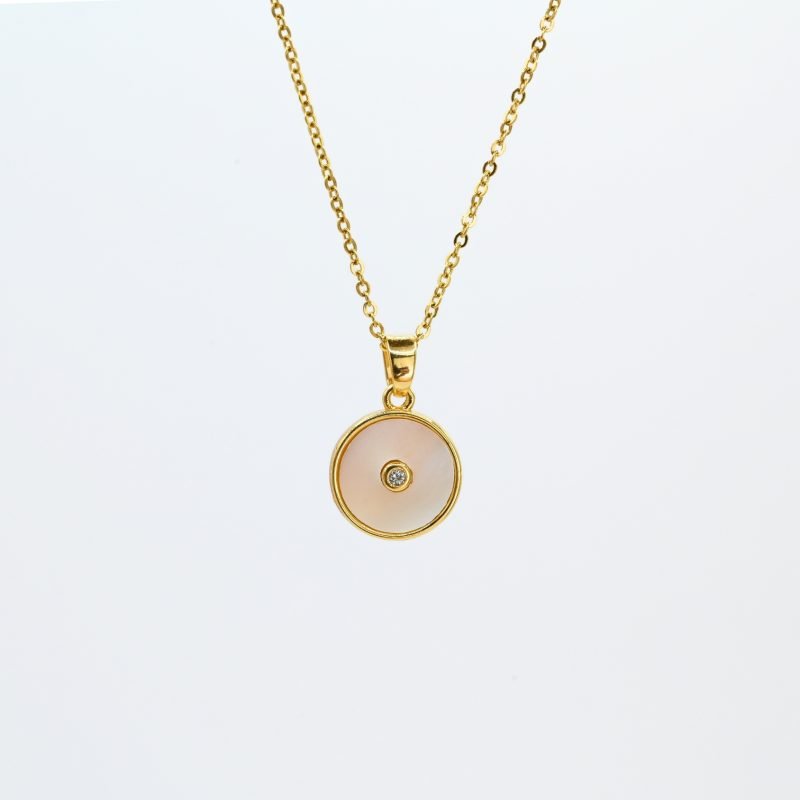 "Collier avec une nacre naturelle montée sur du métal doré à l’or fin 24 carats et cabochon en nacre qui mesure 1 cm de diamètre avec en son centre un petit zircon. La longueur de la chaîne est de 40 cm + chaînette de rallonge. . Bijou seul, Crédit GEMITY"