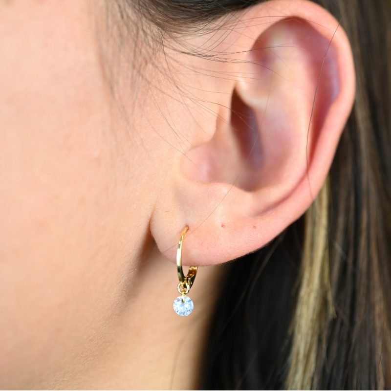 "Boucles d'oreilles en plaqué or avec un zirconium. Vendues par paire. . Bijou porté, Crédit GEMITY."