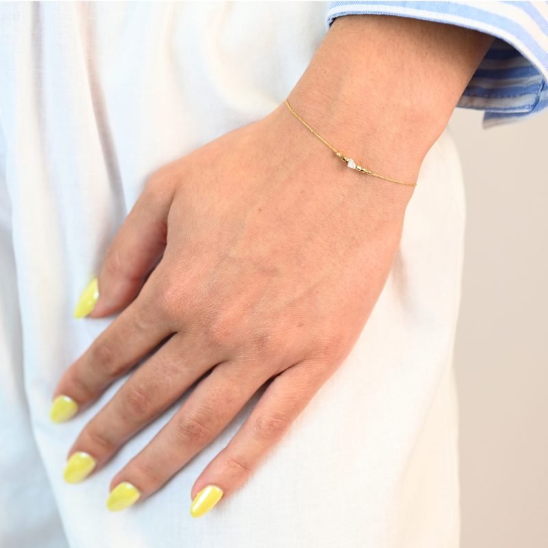"Bracelet plaqué or (3 microns) avec un zirconium, entouré par des petites perles cylindriques en plaqué or, sur chaîne extra fine . Bijou porté, Crédit GEMITY."