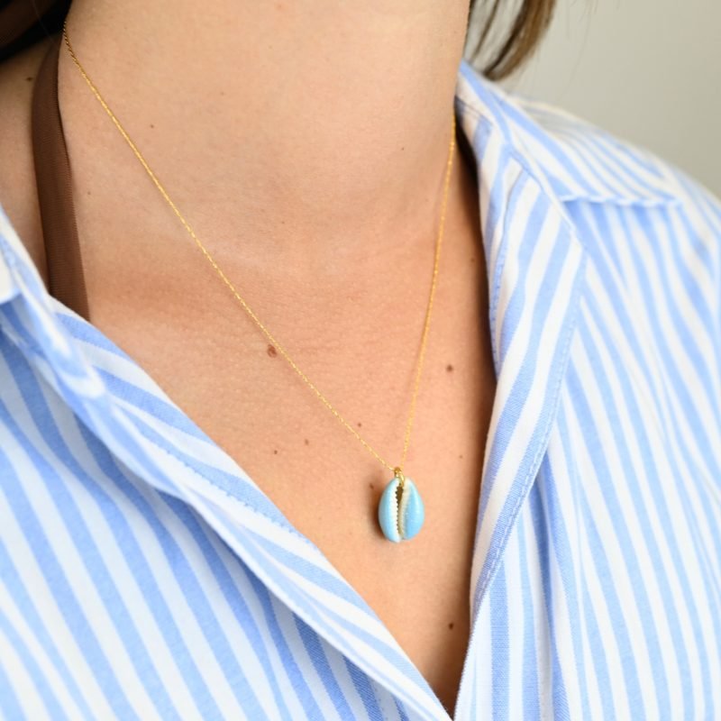"Collier plaqué or (3 microns) coquillage émaillé Véritable cauri (coquillage) d’une longueur d’environ 2 cm Taille de la chaîne : 39 cm (+5cm de chaîne de rappel) . Bijou porté, Crédit GEMITY."