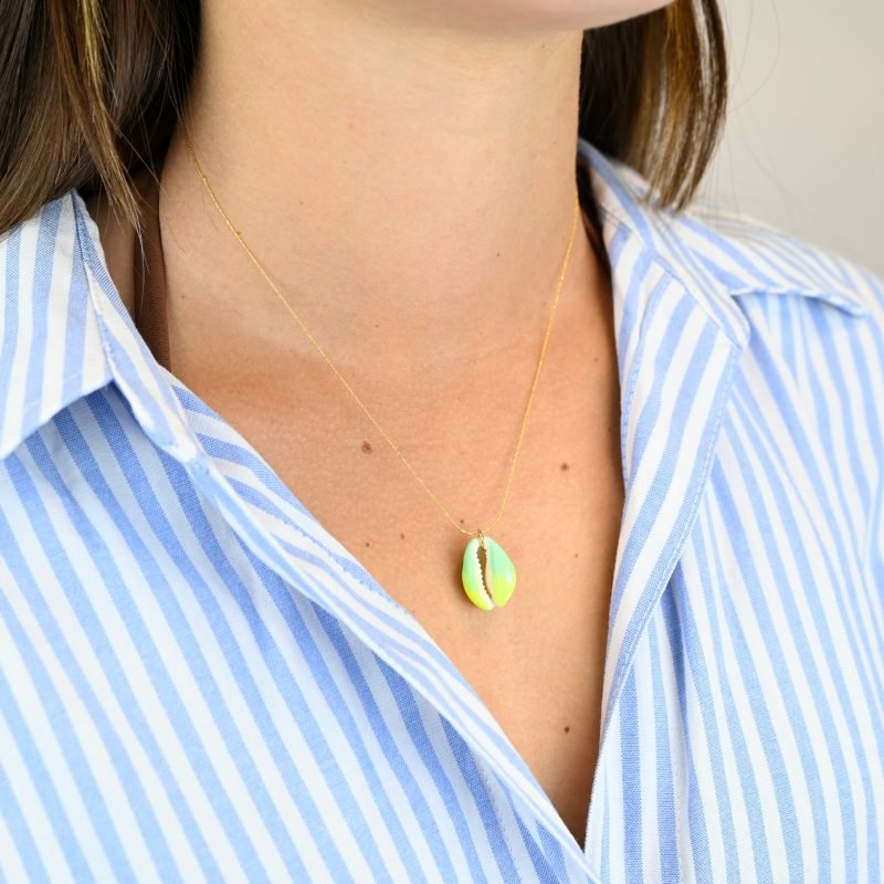 "Collier plaqué or (3 microns) coquillage émaillé Véritable cauri (coquillage) d’une longueur d’environ 2 cm Taille de la chaîne : 39 cm (+5cm de chaîne de rappel) . Bijou porté, Crédit GEMITY."