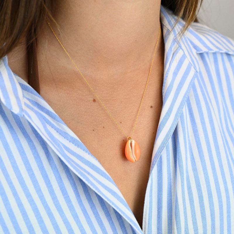 "Collier plaqué or (3 microns) coquillage émaillé Véritable cauri (coquillage) d’une longueur d’environ 2 cm Taille de la chaîne : 39 cm (+5cm de chaîne de rappel) . Bijou porté, Crédit GEMITY."