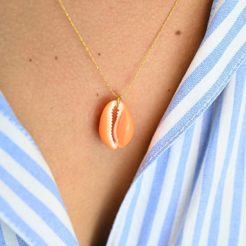 "Collier plaqué or (3 microns) coquillage émaillé Véritable cauri (coquillage) d’une longueur d’environ 2 cm Taille de la chaîne : 39 cm (+5cm de chaîne de rappel) . Bijou porté, Crédit GEMITY."